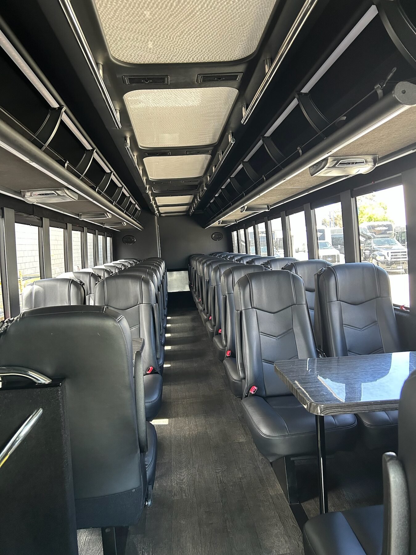 Interior of a corporate coach bus with rows of forward-facing leather seats and tray tables